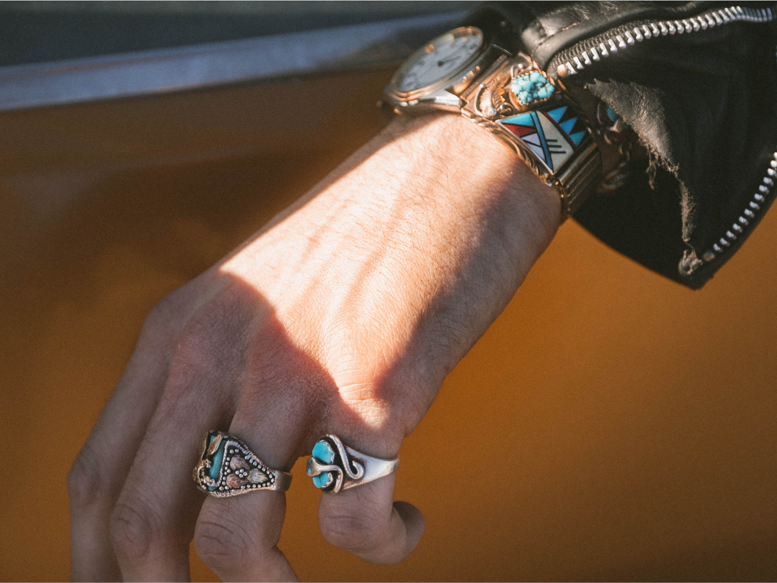 a hand resting on a car door showcasing sevearl rings and a matching watch.